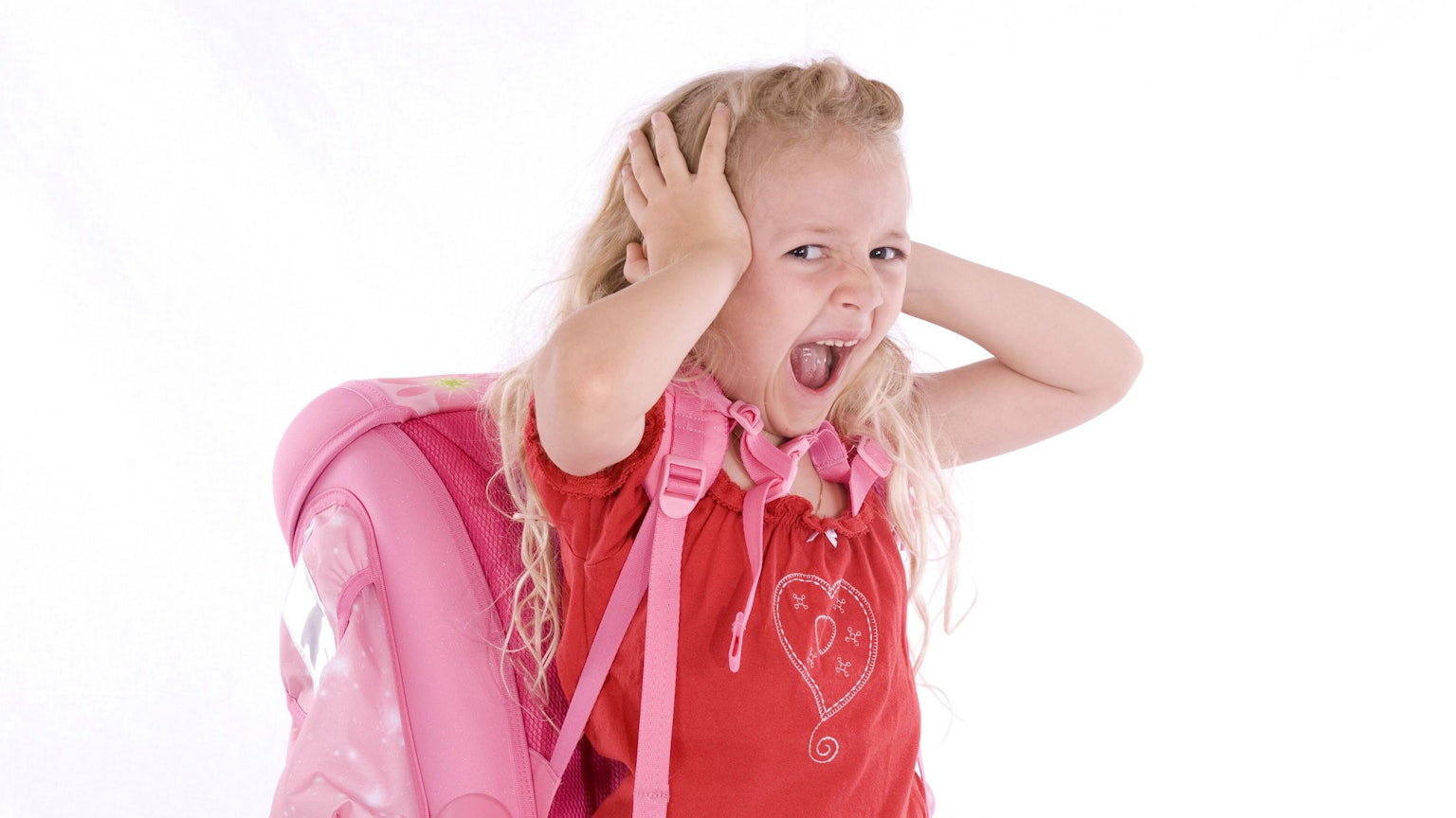 Ein überfordertes Mädchen mit Schulranzen schreit und hält sich die Ohren zu.
