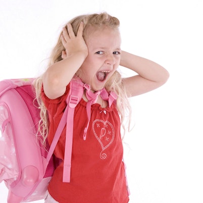 Ein überfordertes Mädchen mit Schulranzen schreit und hält sich die Ohren zu.
