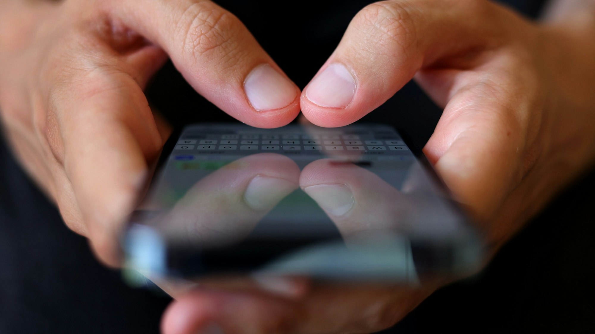 Ein junger Mann tippt auf einem Smartphone eine WhatsApp-Nachricht.