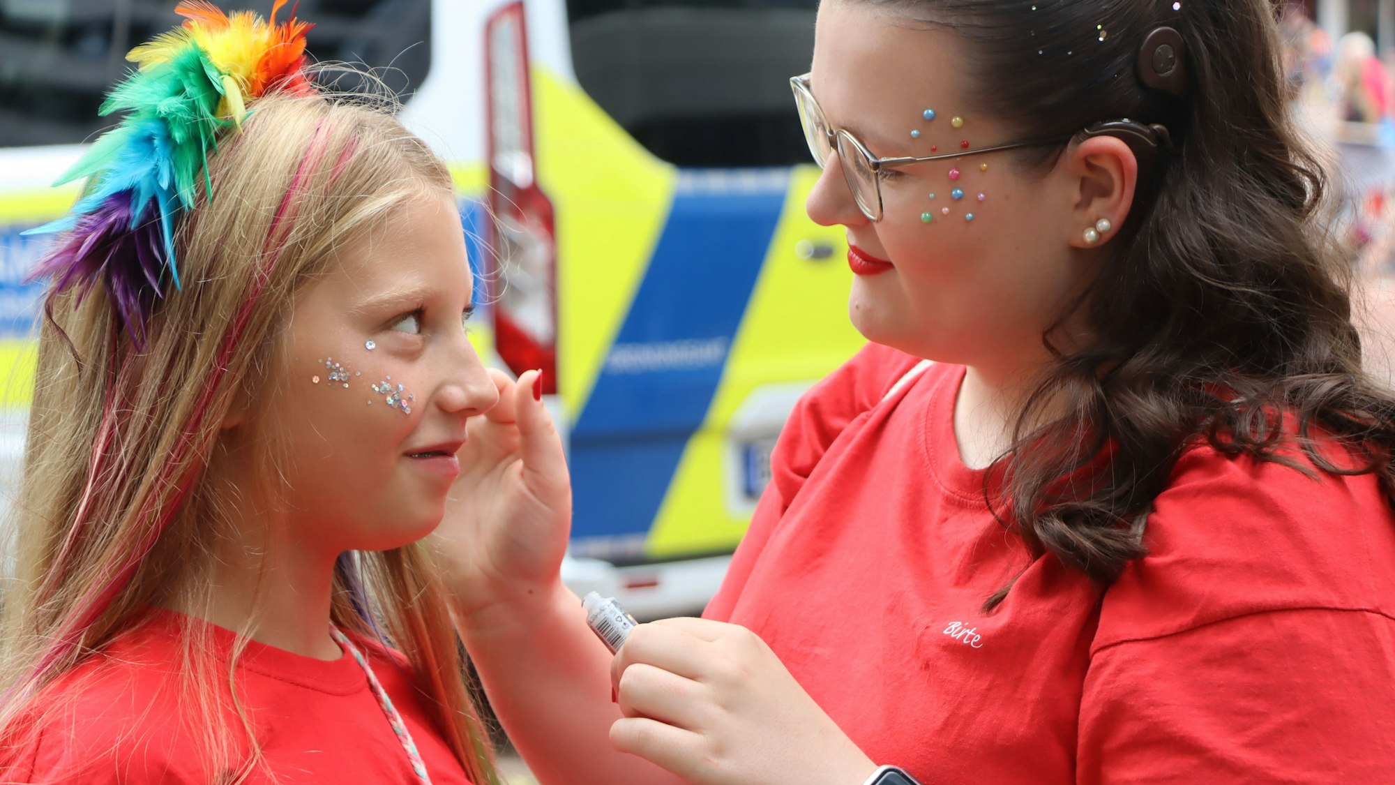 Zu sehen ist eine Frau, die ein Mädchen schminkt.