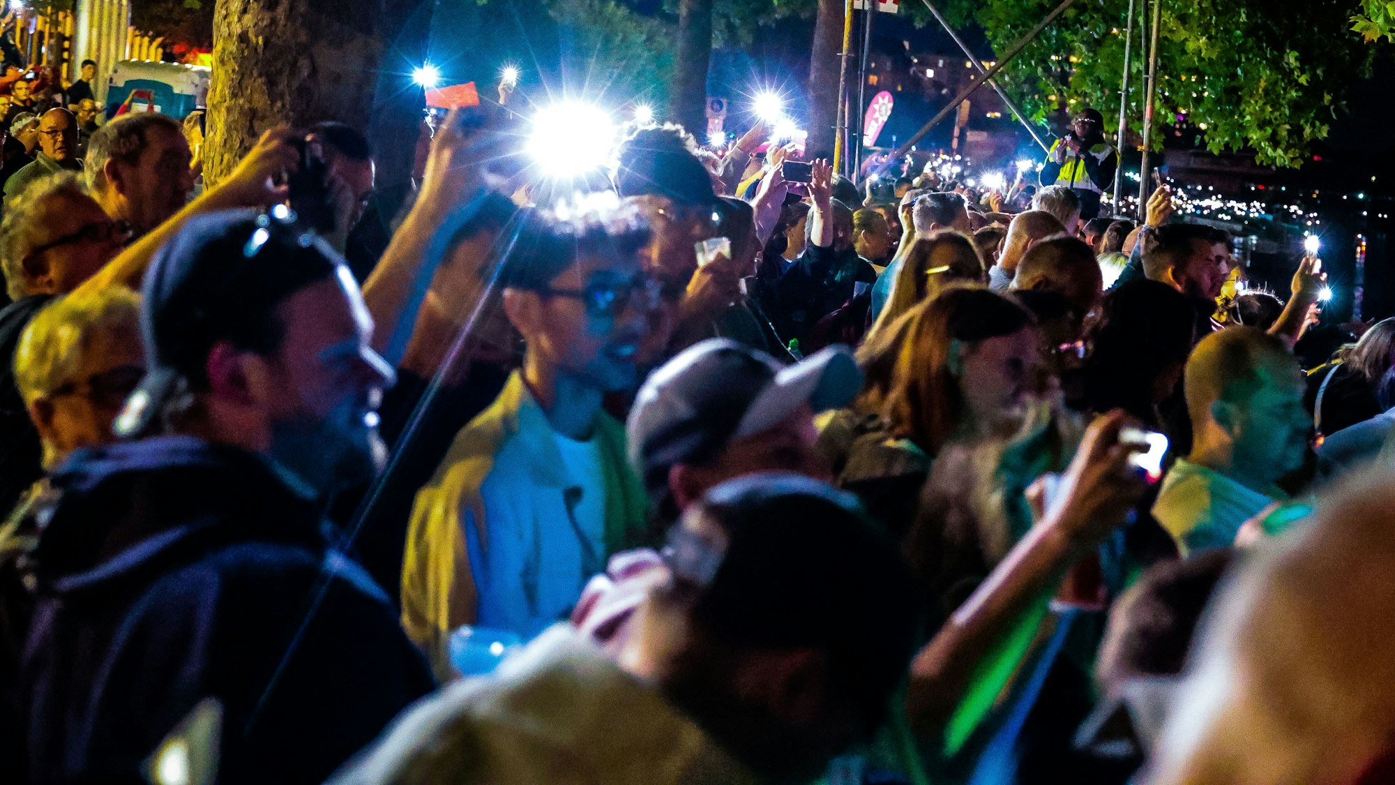 Das Bild zeigt Zuschauer am Rheinufer, die mit Handytaschenlampen leuchten.