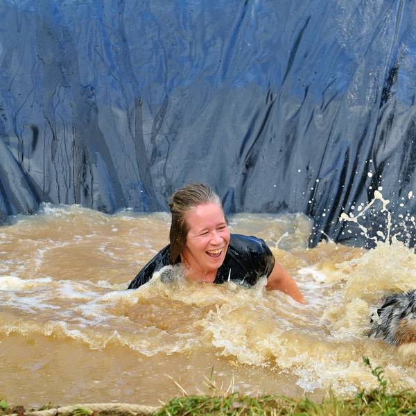 Eine Frau im Wasser schaut lachend auf einen Hund.