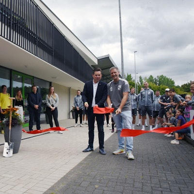 Zwei Männer mit Scheren in der Hand vor einem großen Zweckbau.