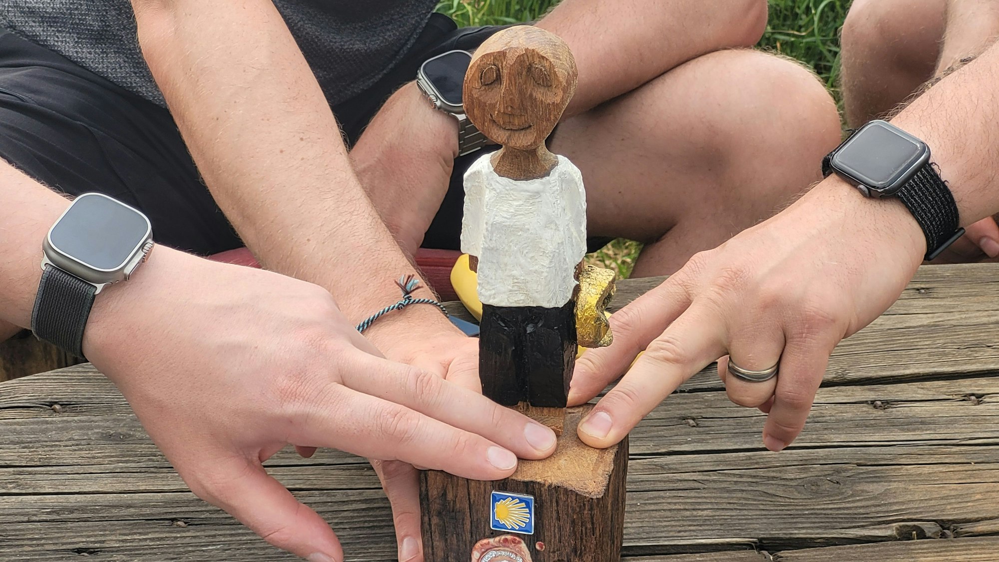 Das Bild zeigt die Holzskulptur und die Hände von Menschen, die den Sockel der Figur berühren.