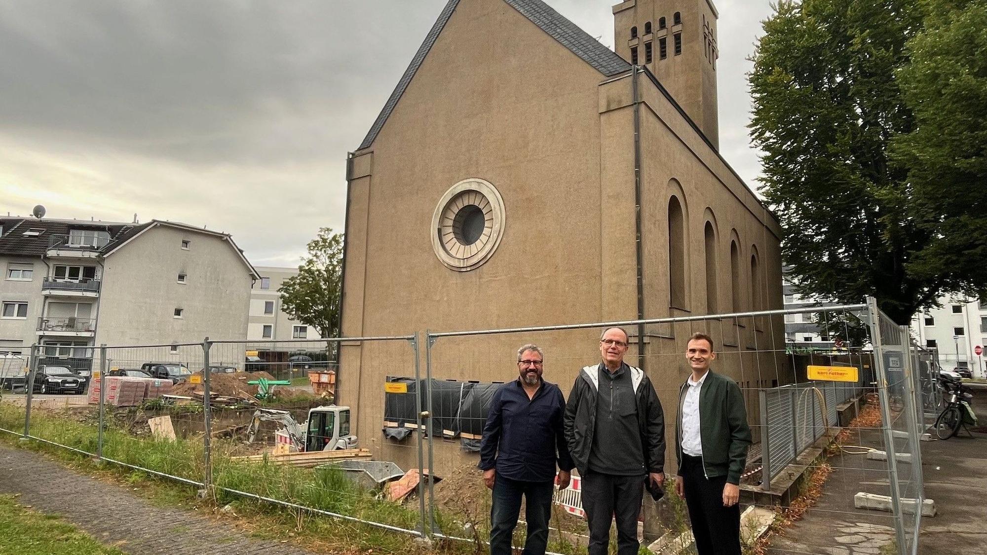 Drei Männer stehen vor einer eingezäunten Kirche.