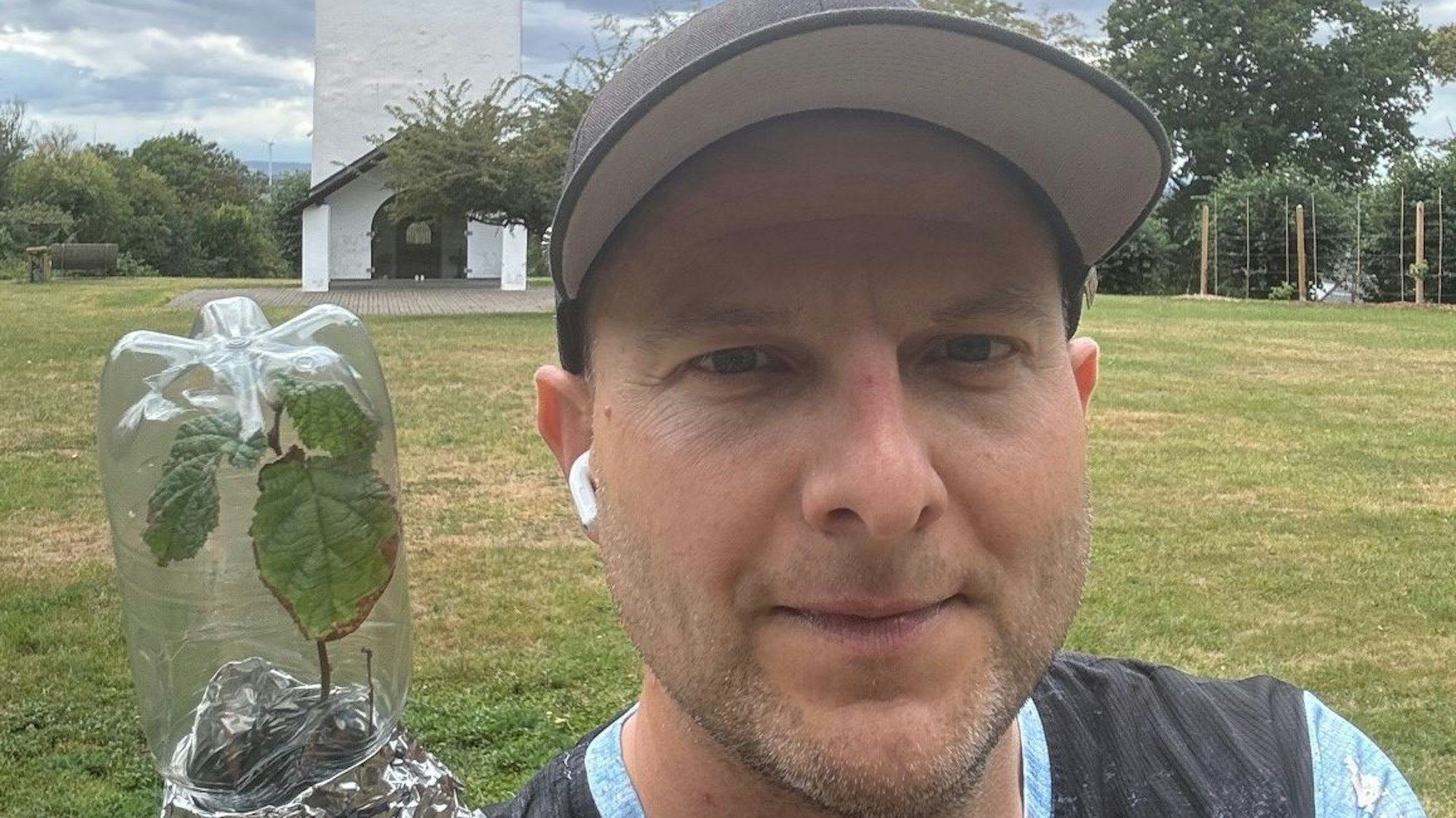 Das Bild zeigt Matthias Stupp vor dem Swister Turm in Weilerswist. Er trägt eine Kappe und hat den Hasselnussbaum-Setzling in der Hand.