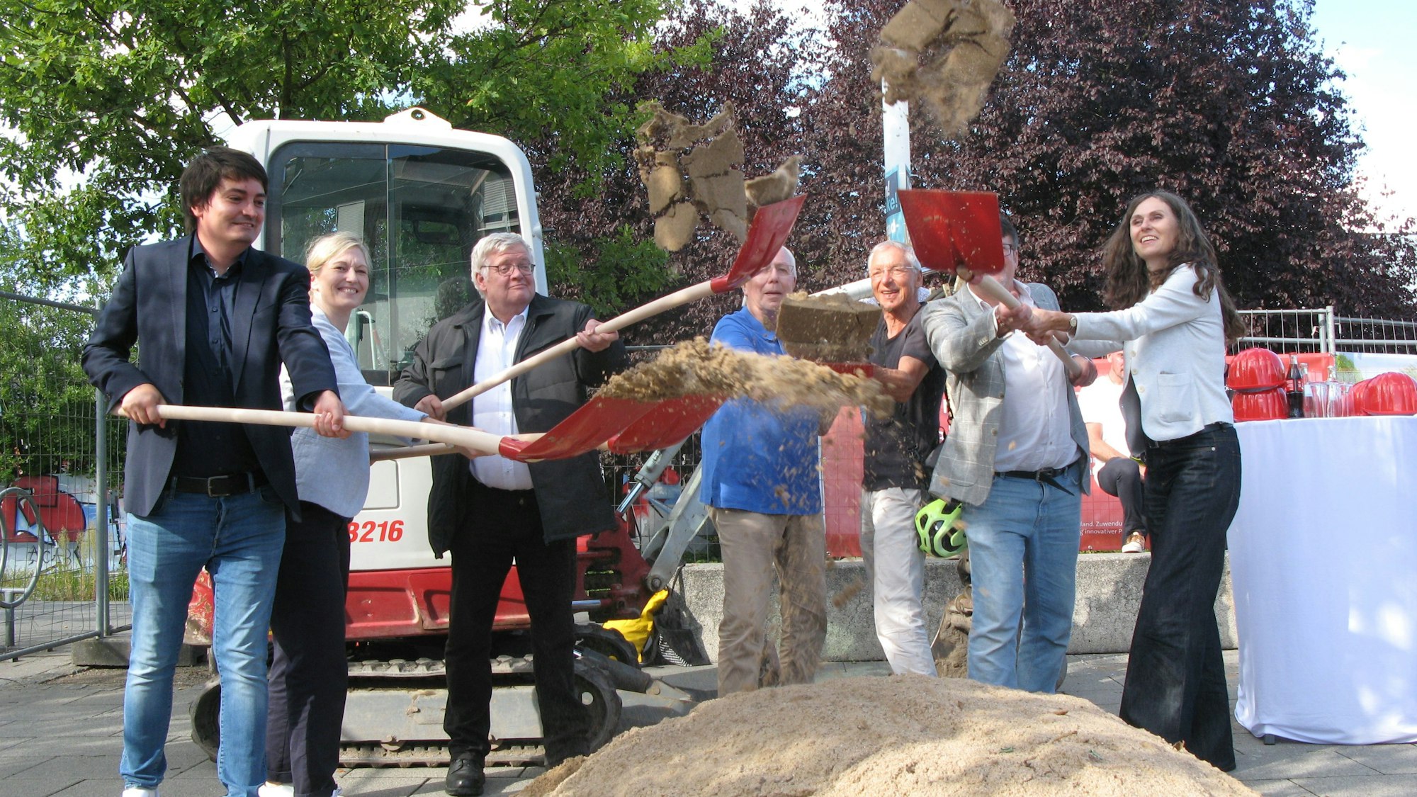 Fünf Männer und zwei Frauen werfen mit Schaufeln Sand in die Luft.