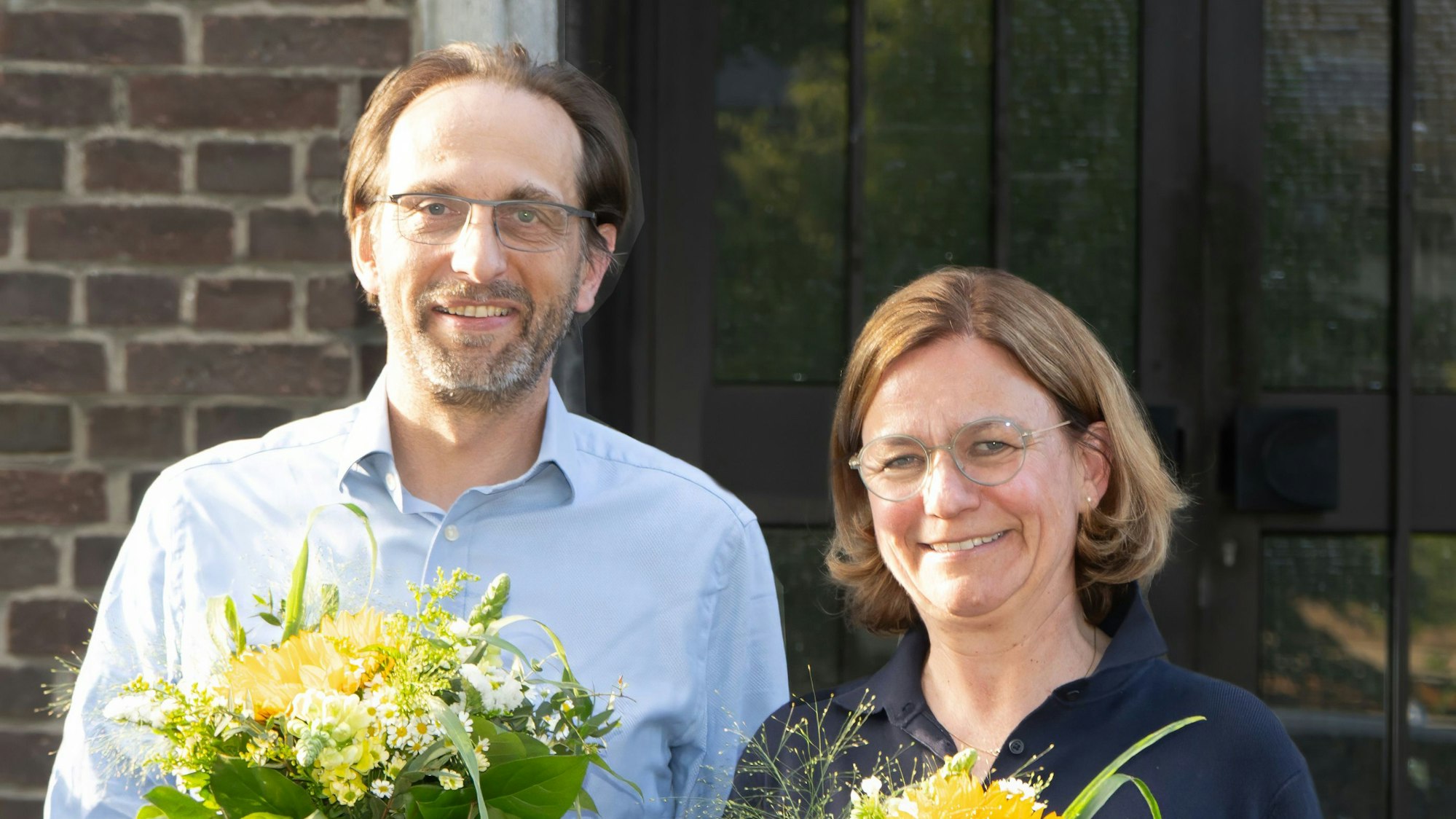 Auf dem Bild sind ein Mann und eine Frau zu sehen, sie halten Blumensträuße in der Hand.