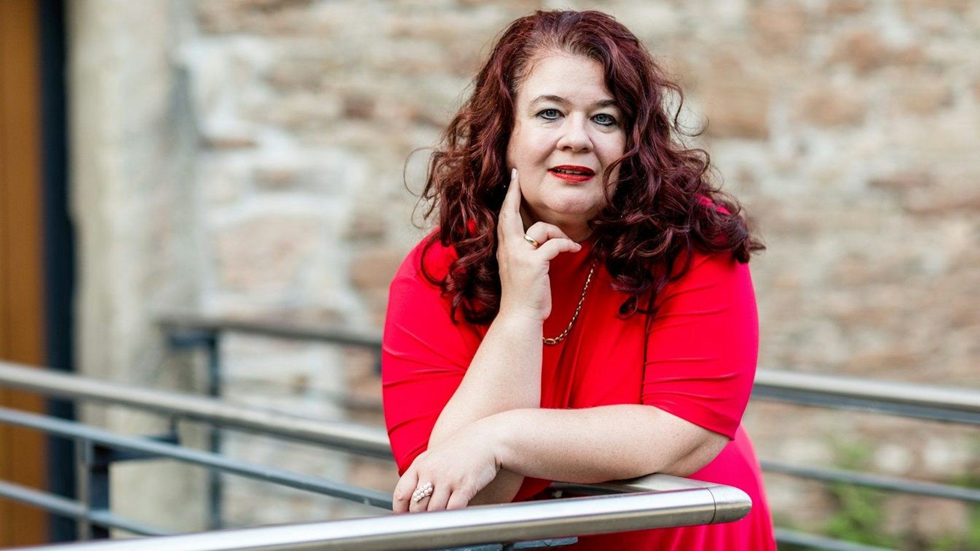 Eine Frau im roten Kleid lehnt auf einem Geländer.