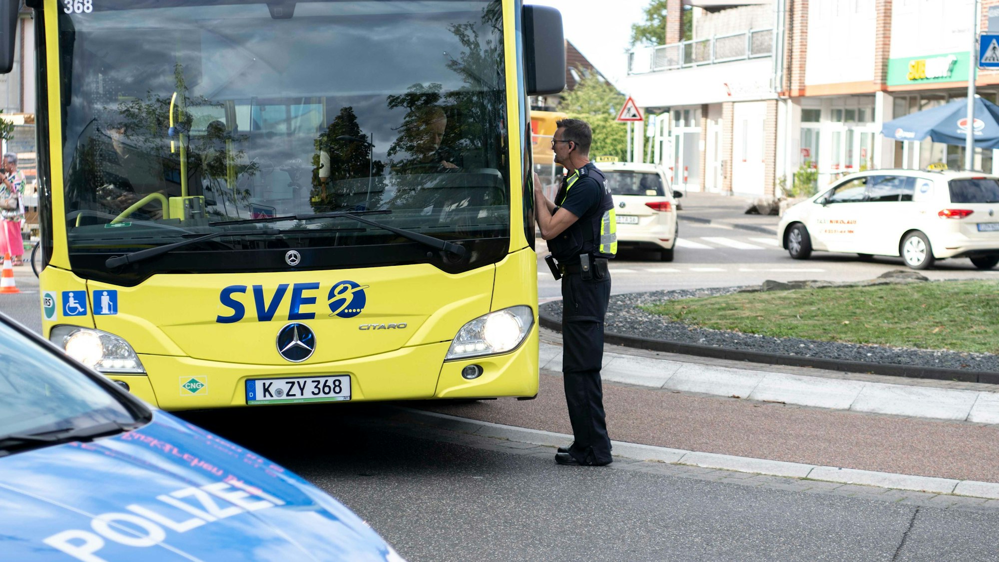 Das Bild zeigt einen Polizisten, der einem Busfahrer erklärt, dass die Straße gesperrt ist.