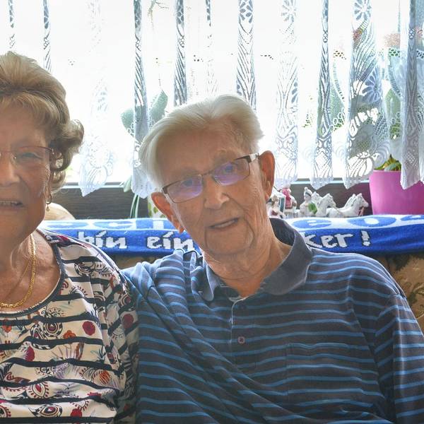Gertrud Elisabeth und Rudolf Pohl sitzen vor einem hellen Vorhang, durch den Licht scheint. Er hält seinen rechten Arm um sie.