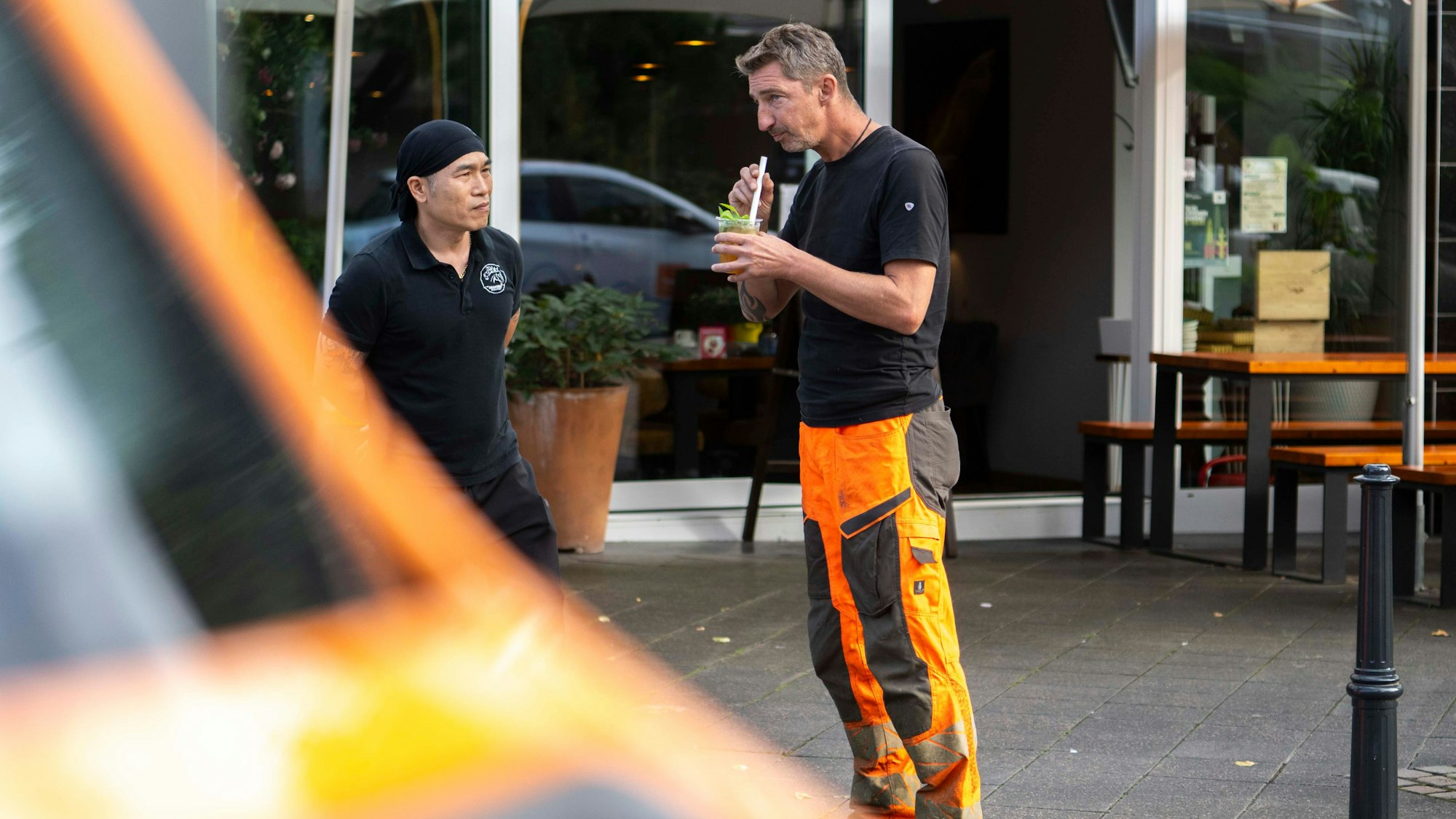 Das Bild zeigt einen Mitarbeiter der Technischen Dienste in Euskirchen, der von einem Mitarbeiter eines Restaurants ein Getränk erhalten hat.