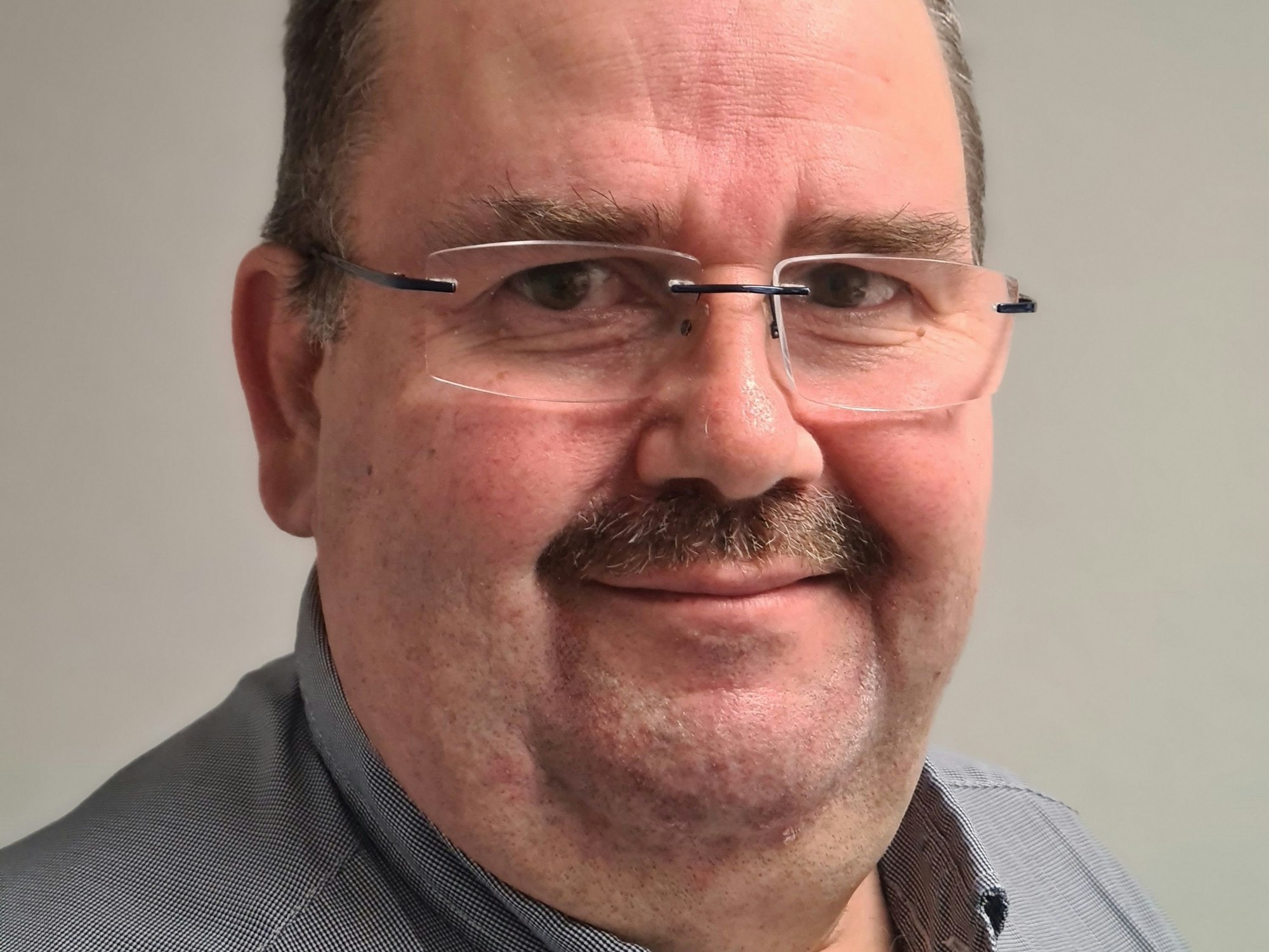 Linke trägt ein graues Hemd und eine Brille.