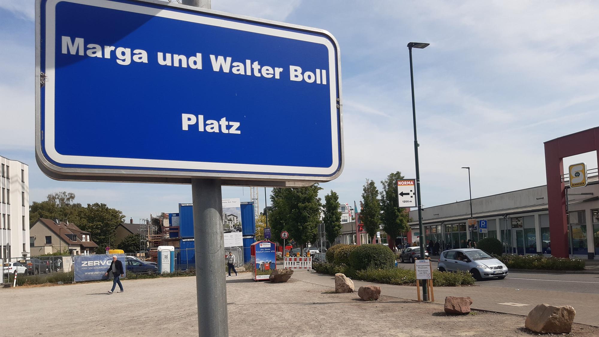 Das Bild zeigt ein Schild mit der Aufschrift „Marga-und-Walter-Boll-Platz“, im Hintergrund der recht kahle Platz.