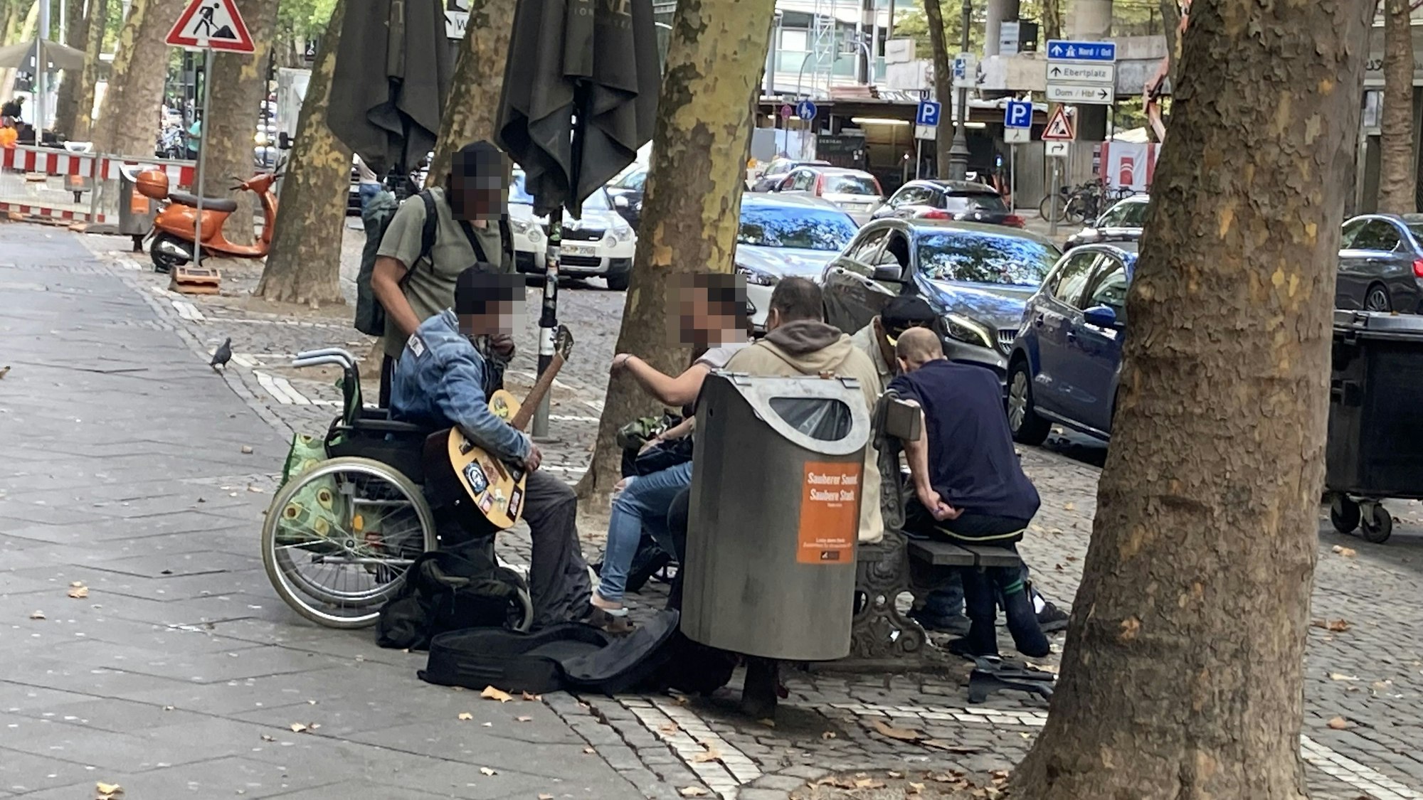 Menschen sitzen auf und um eine Bank am Hohenzollernring herum