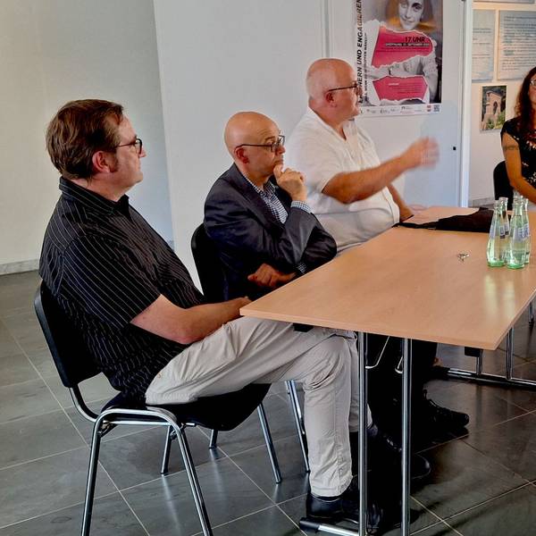 Sechs Menschen sitzen zusammen an einer Tischgruppe und diskutieren.