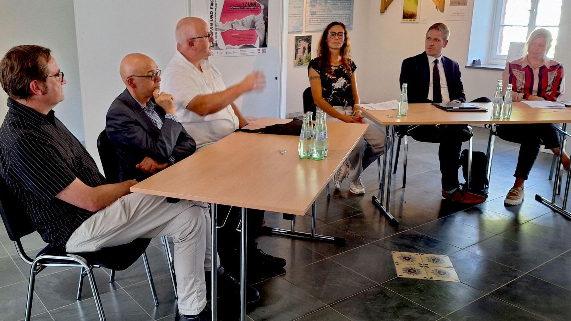 Sechs Menschen sitzen zusammen an einer Tischgruppe und diskutieren.
