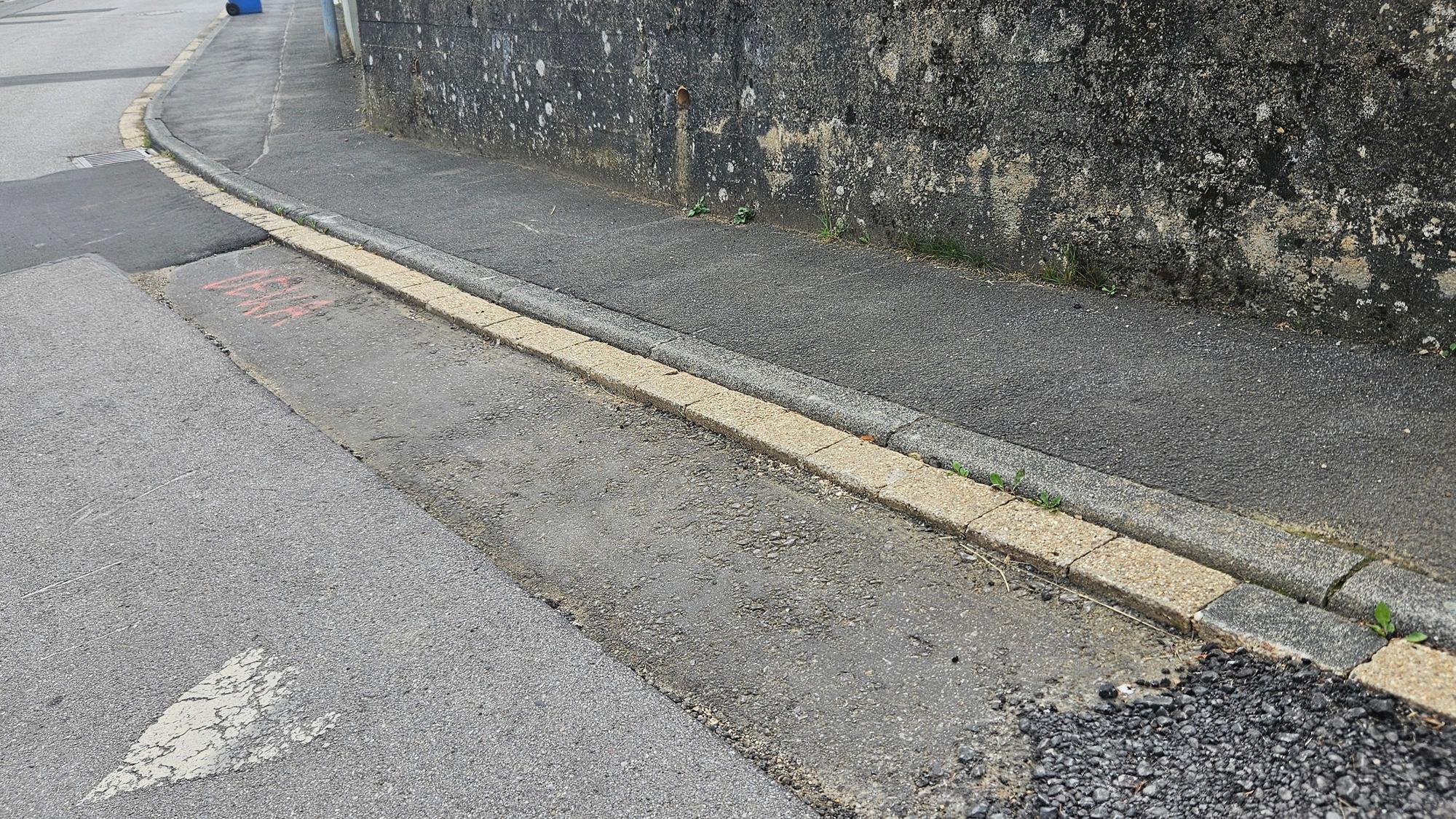 Das Foto zeigt einen Streifen am Straßenrand, bei dem die oberste Asphaltschicht fehlt.