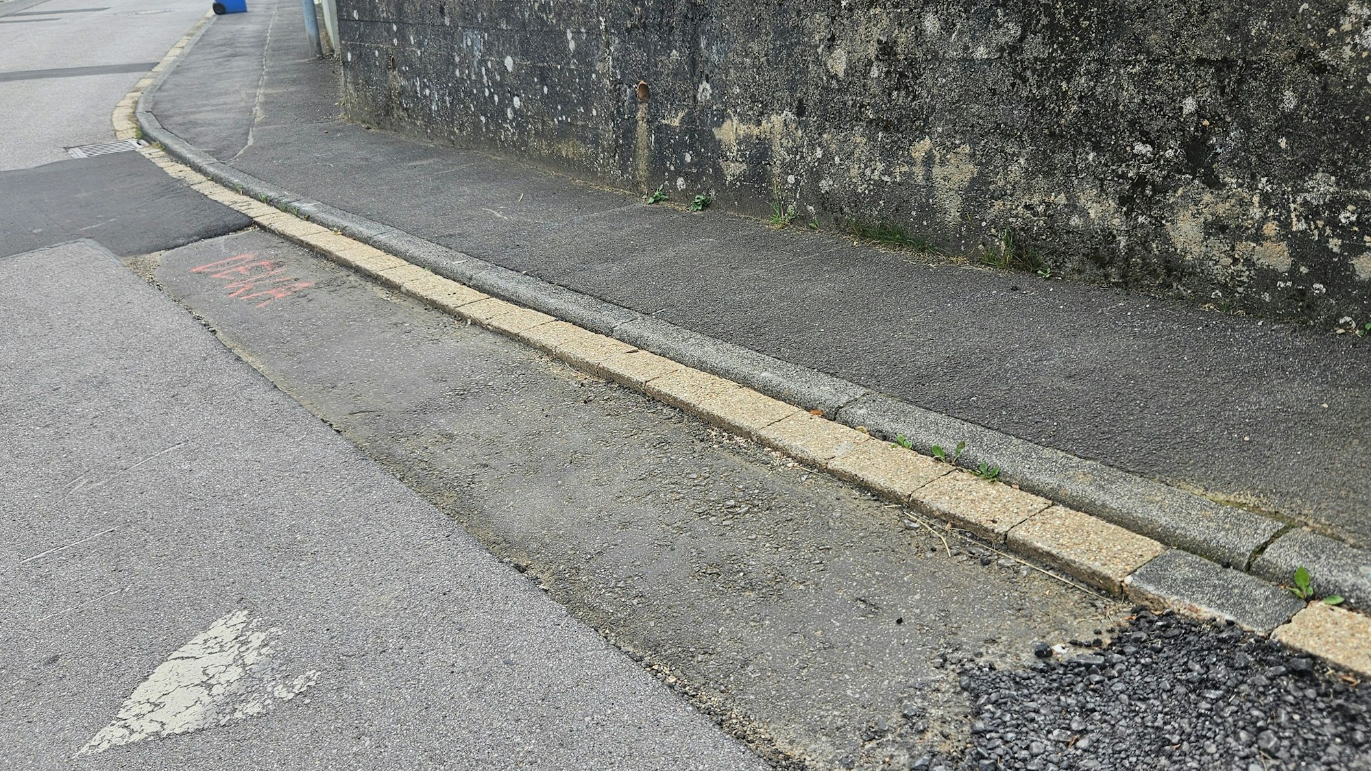 Das Foto zeigt einen Streifen am Straßenrand, bei dem die oberste Asphaltschicht fehlt.