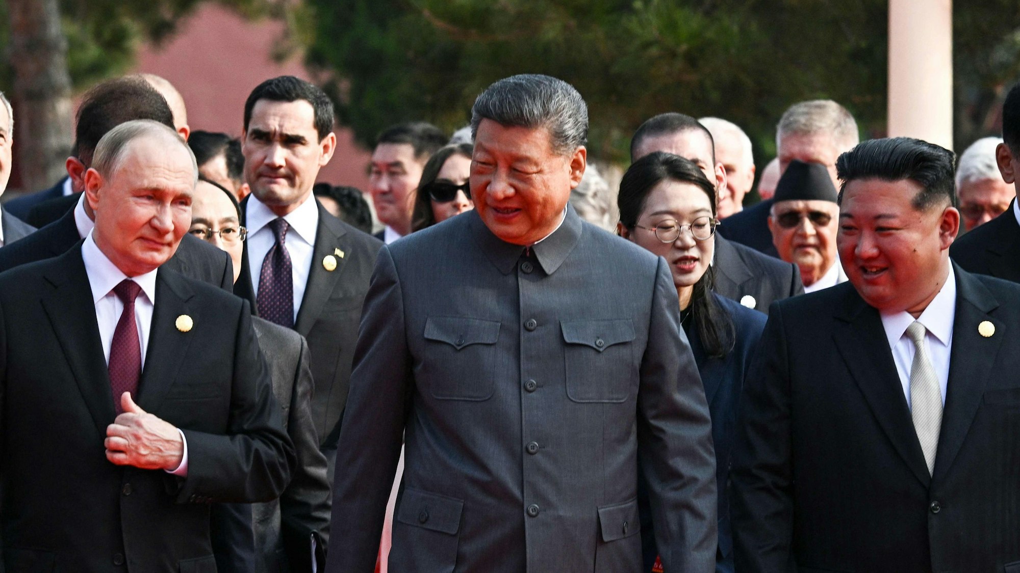 Putin, Xi und Kim gehen lächelnd nebeneinander her.