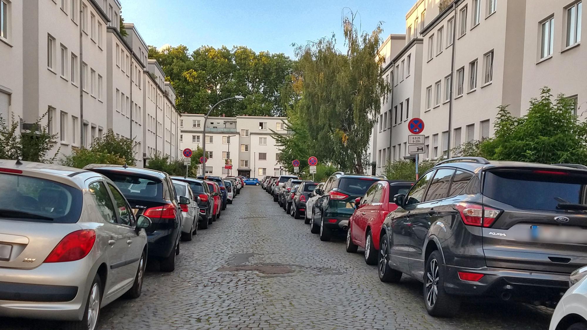 Eine enge, lange Straße, auf der links und rechts viele Autos parken.