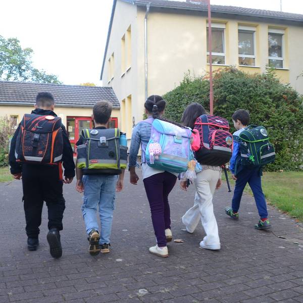 Grundschulkinder laufen auf ein Schulgebäude zu.