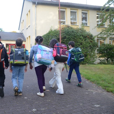 Grundschulkinder laufen auf ein Schulgebäude zu.