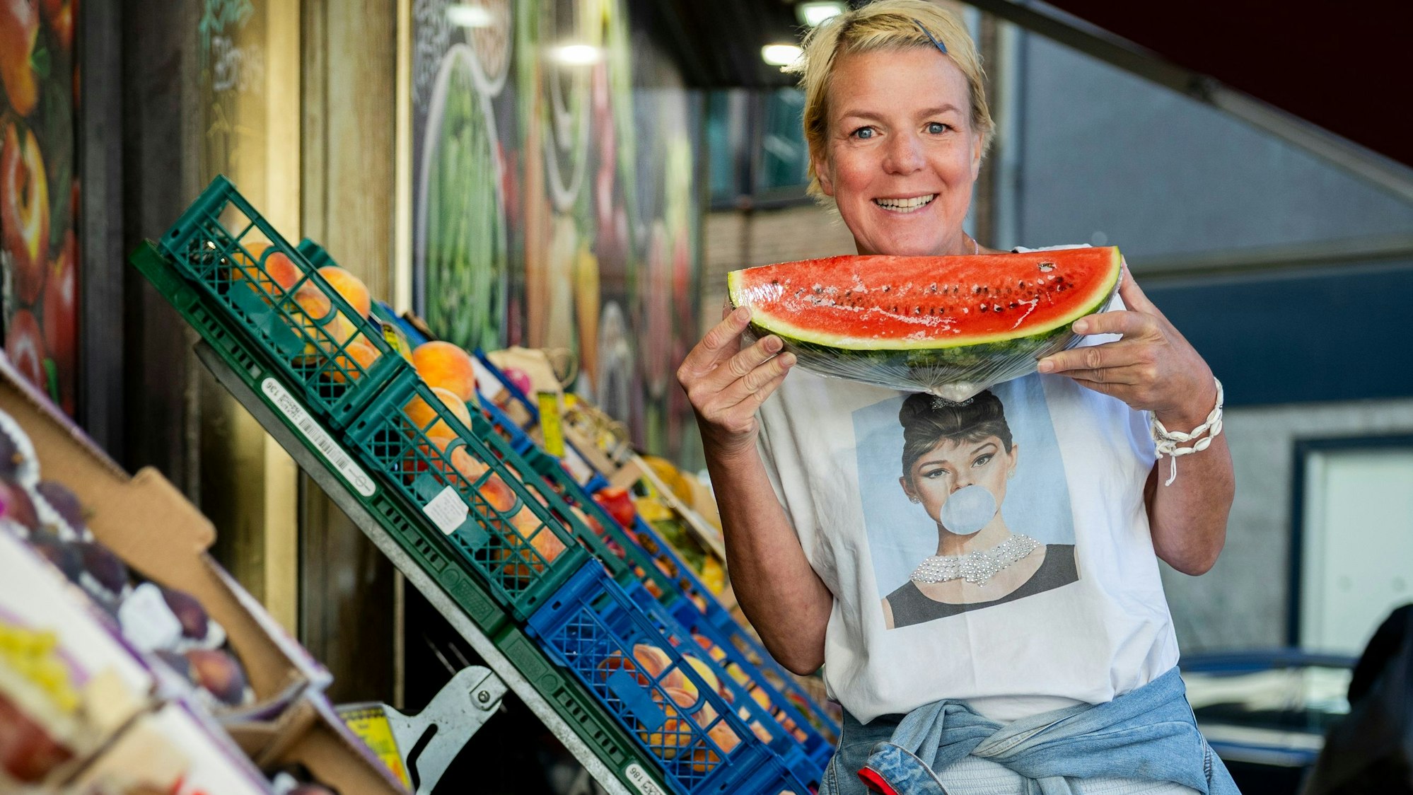 Eine Frau hält eine Wassermelone und grinst.