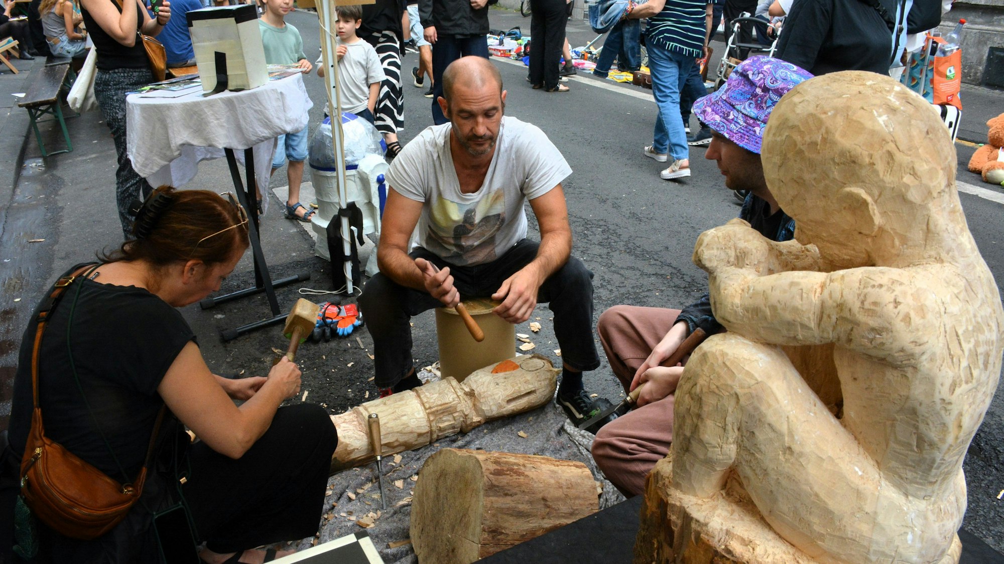 Zwei Personen üben sich bei einem Straßenfest im Skulpturenschnitzen.