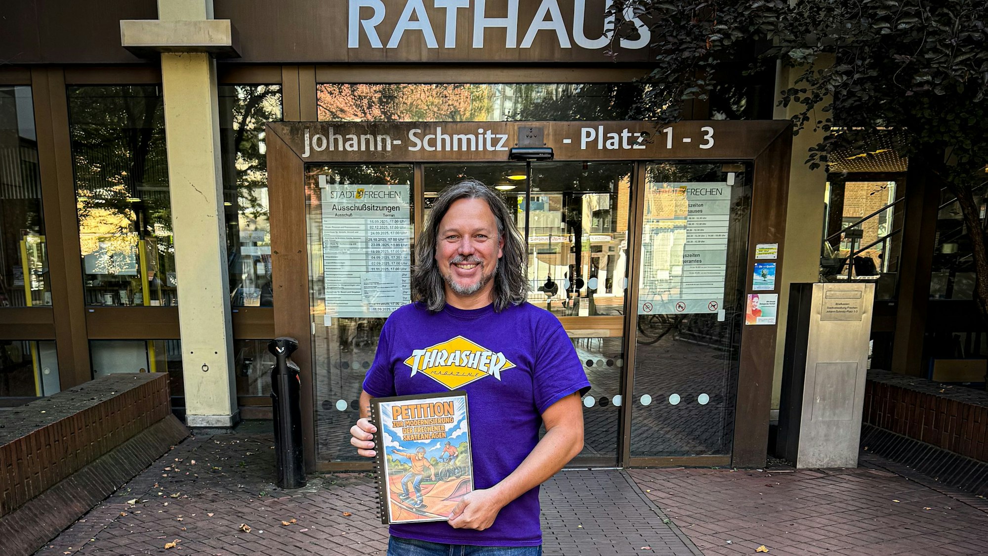 Auf dem Bild ist ein Mann vor dem Rathaus zu sehen, er hat eine Unterschriftenmappe in der Hand.