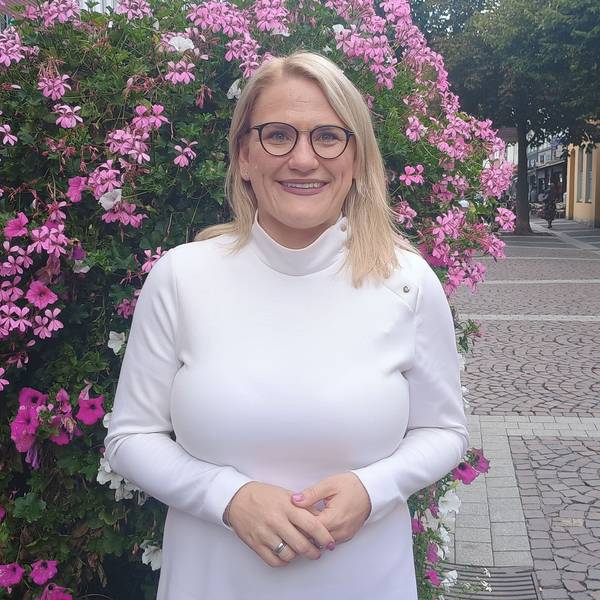 Christina Stumpp steht in der Brühler Innenstadt vor einem blumigen Busch. Sie trägt ein weißes Oberteil und eine Brille.