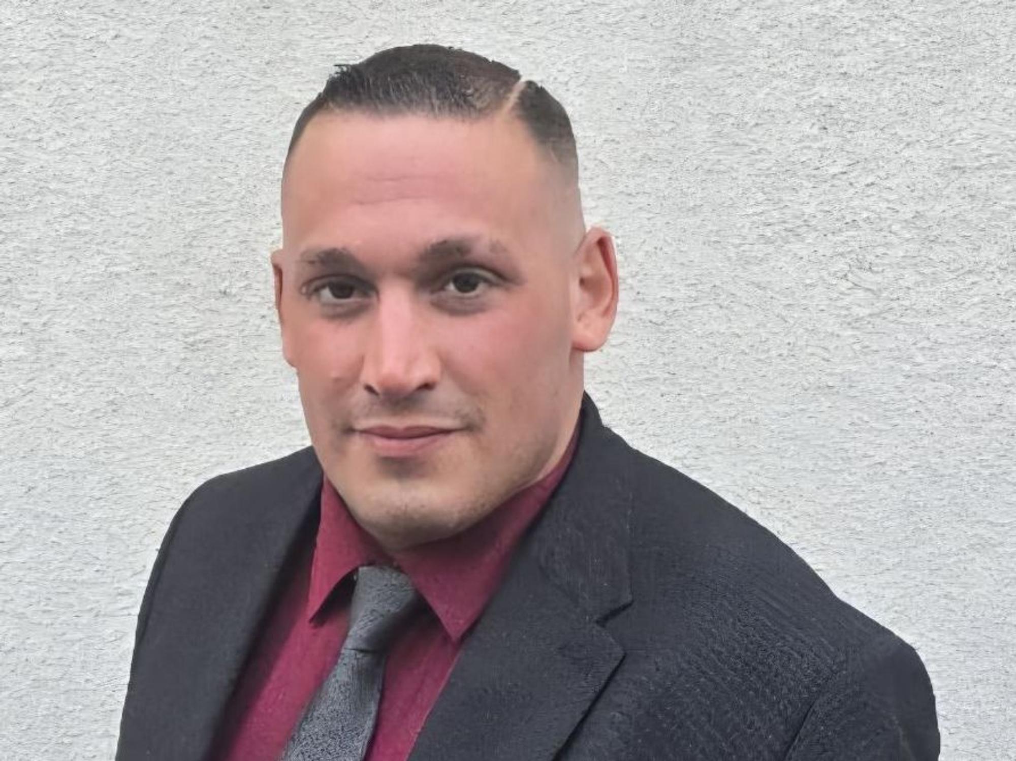 Simon Müller steht im Anzug vor einer Wand.