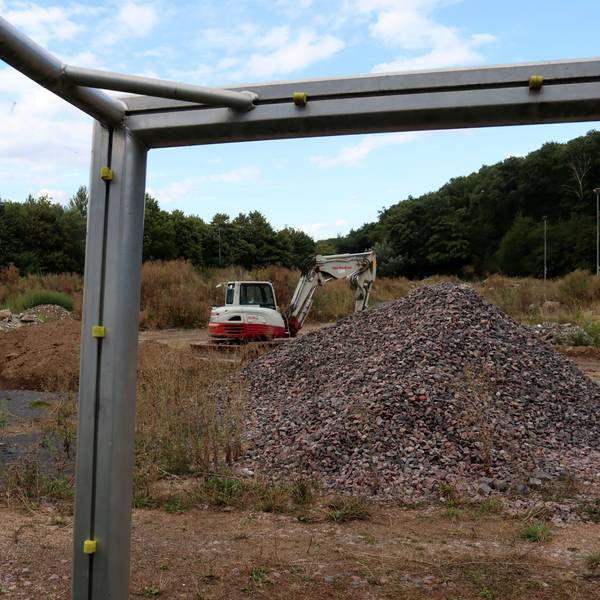Das Bild zeigt den Sportplatz in Bad Münstereifel, der seit der Flutkatastrophe als Ablagestätte für Schutt genutzt wird. Das Foto wurde durch das Fußballtor hindurch gemacht, im Torwinkel befindet sich ein Bagger.