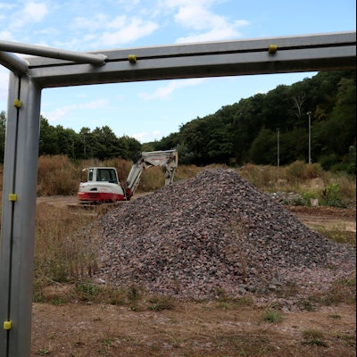 Das Bild zeigt den Sportplatz in Bad Münstereifel, der seit der Flutkatastrophe als Ablagestätte für Schutt genutzt wird. Das Foto wurde durch das Fußballtor hindurch gemacht, im Torwinkel befindet sich ein Bagger.