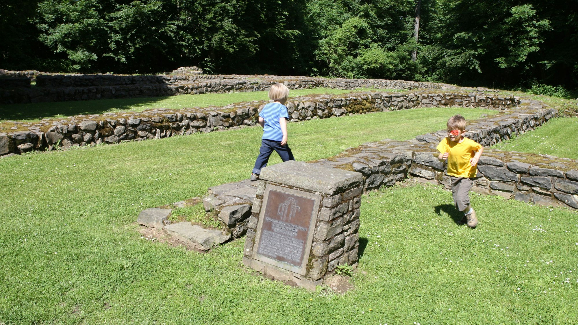 Kinder spielen auf dem Rasen zwischen Grundmauern einer historischen Klosterkirche.