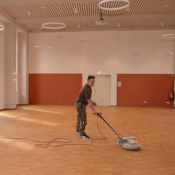 Ein Mann poliert neu gelegtes Parkett mit einer Bohnermaschine.