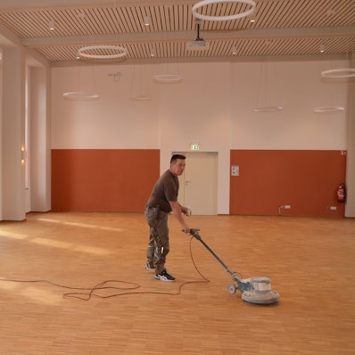 Ein Mann poliert neu gelegtes Parkett mit einer Bohnermaschine.