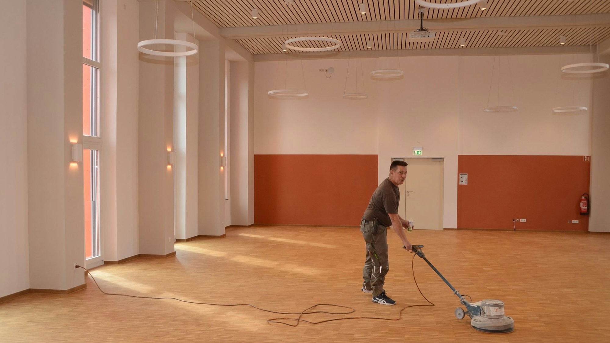 Ein Mann poliert neu gelegtes Parkett mit einer Bohnermaschine.