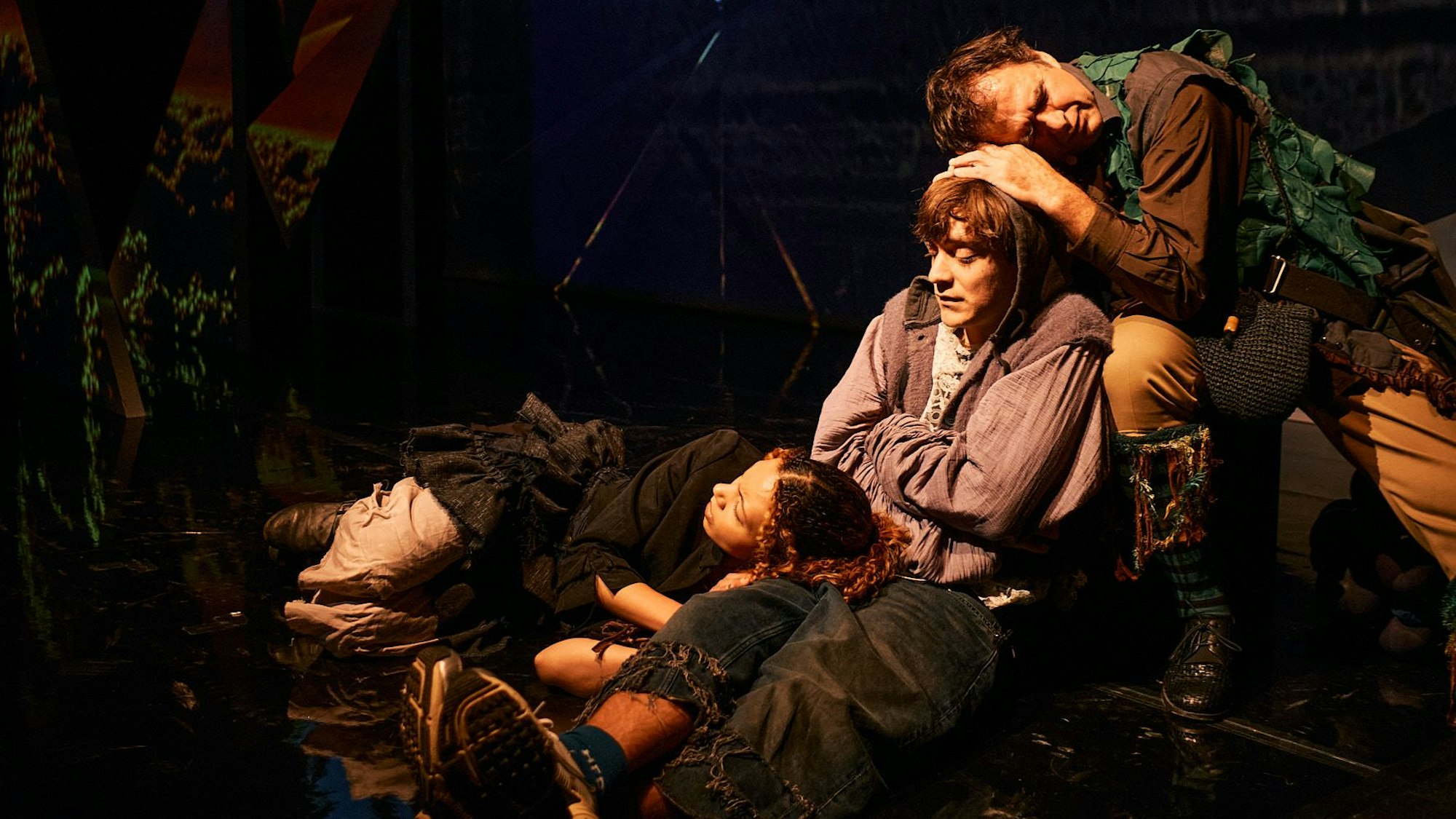 Drei Schauspielende in mittelalterlichen Kostümen lehnen sich zur Rast aneinander.