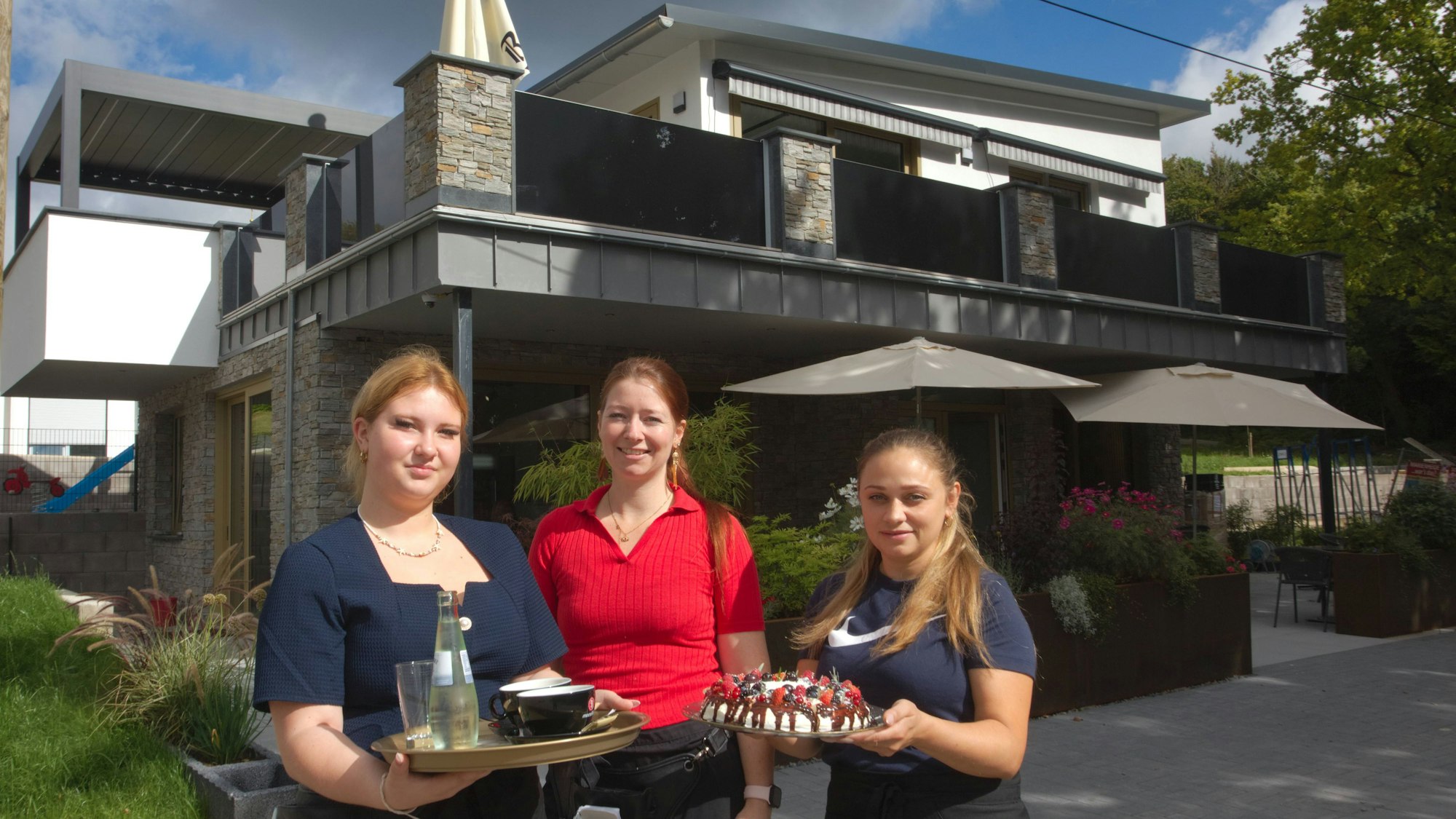 Das Foto zeigt das neue Cafe im Hintergrund, davor stehen drei Frauen.