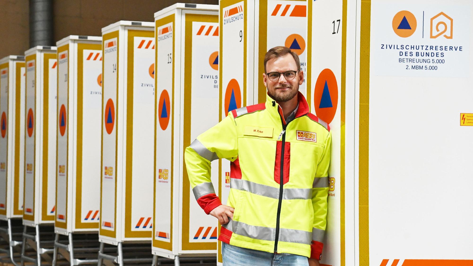 Maximilian Erke lehnt an einem Container mit der Aufschrift Zivilschutz des Bundes; hinter ihm ist eine lange Reihe davon zu sehen. Foto: Alexander Schwaiger