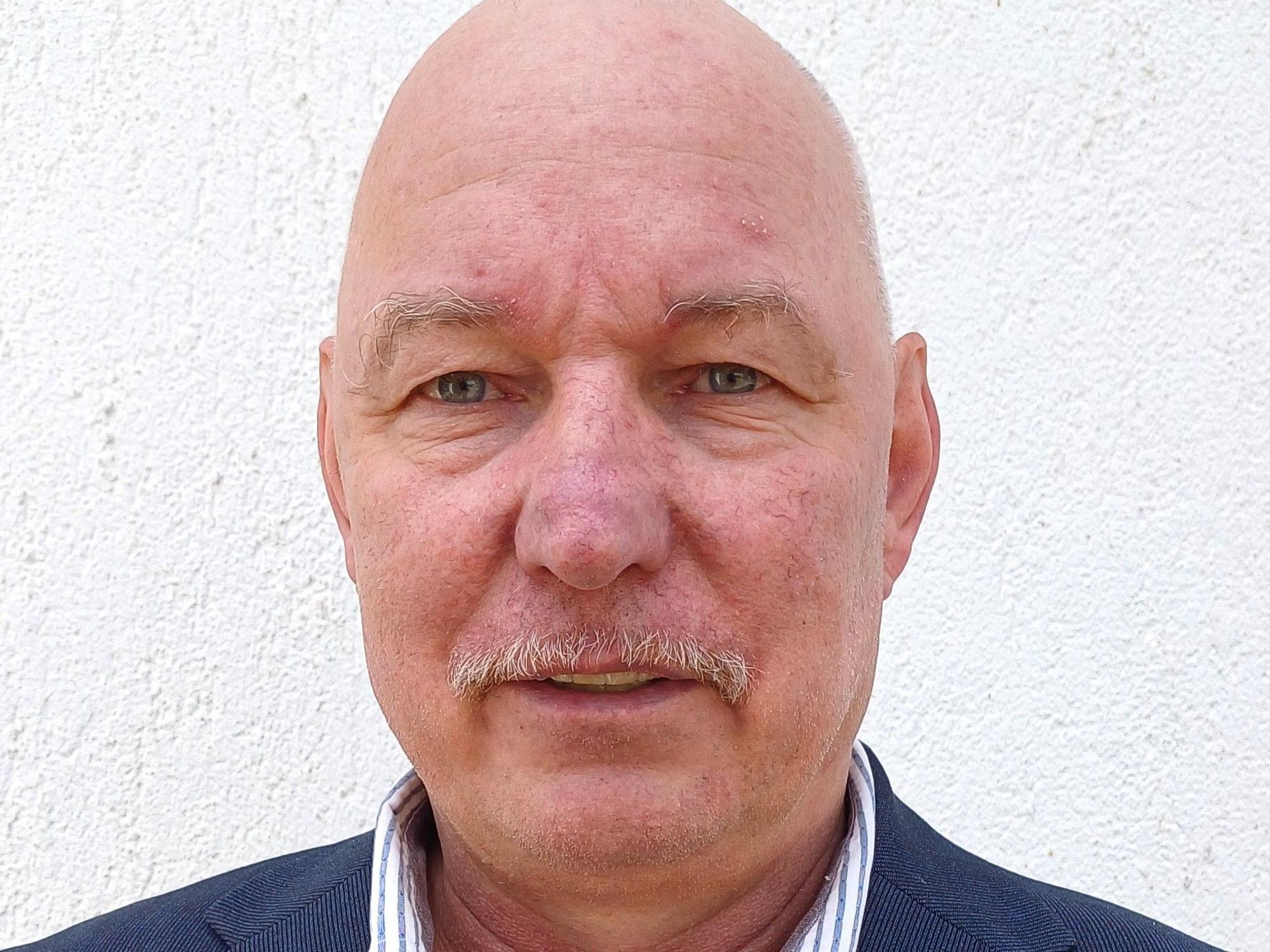 Porträtbild von Harry Deutsch. Er trägt ein Hemd mit hellblauen Streifen und ein Sakko.
