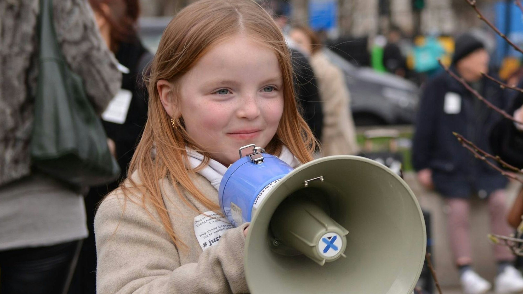 Ein Mädchen mit roten Haaren nimmt mit einem Megafon in den Händen an einer Demo teil.