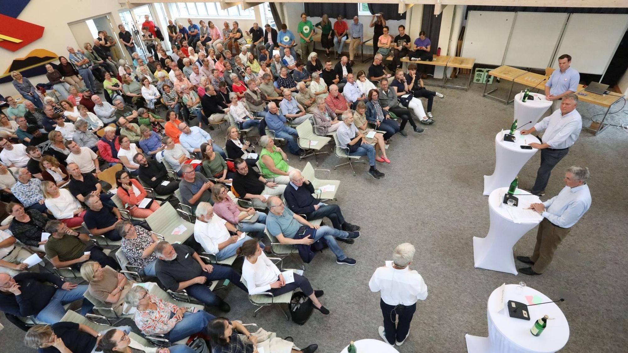 Ein Saal mit vielen Menschen, die auf Stühlen sitzen.