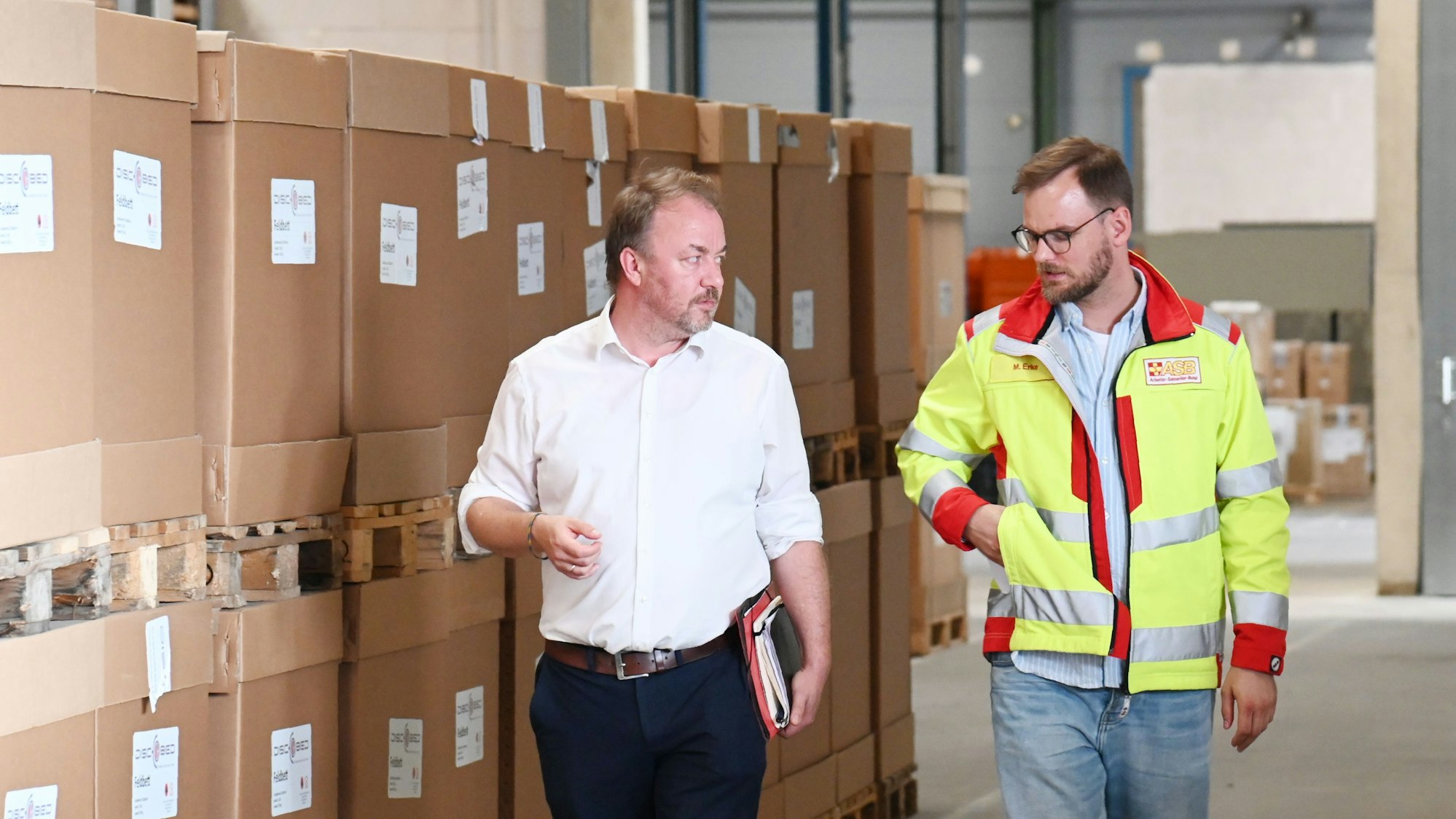 Die beiden Männer gehen an einer langen Reihe brauner Pappkartons entlang und sind im Gespräch. Foto:Alexander Schwaiger