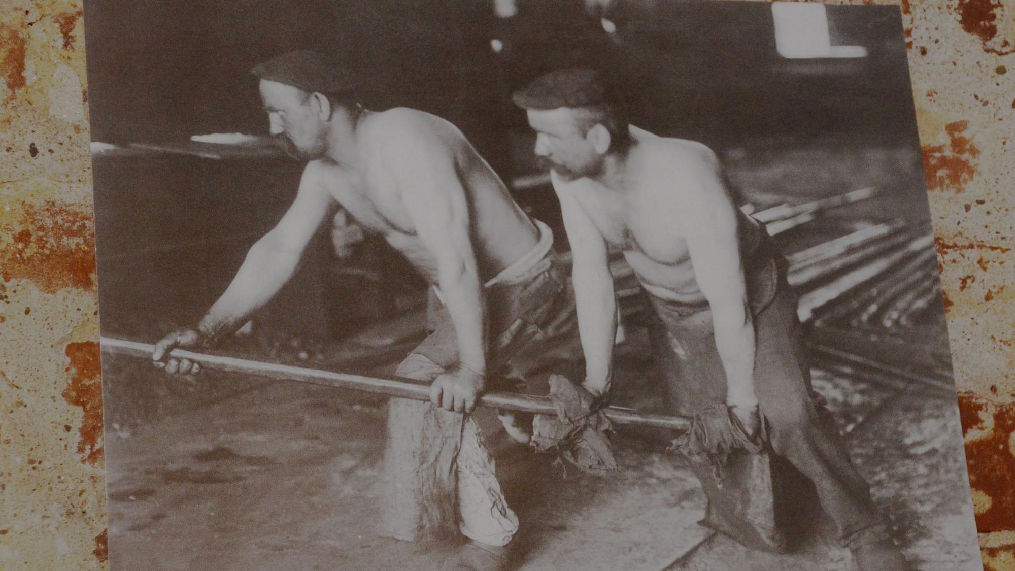 Eine historische Aufnahme zeigt Männer mit freiem Oberkörper bei der Arbeit in einer Fabrik.
