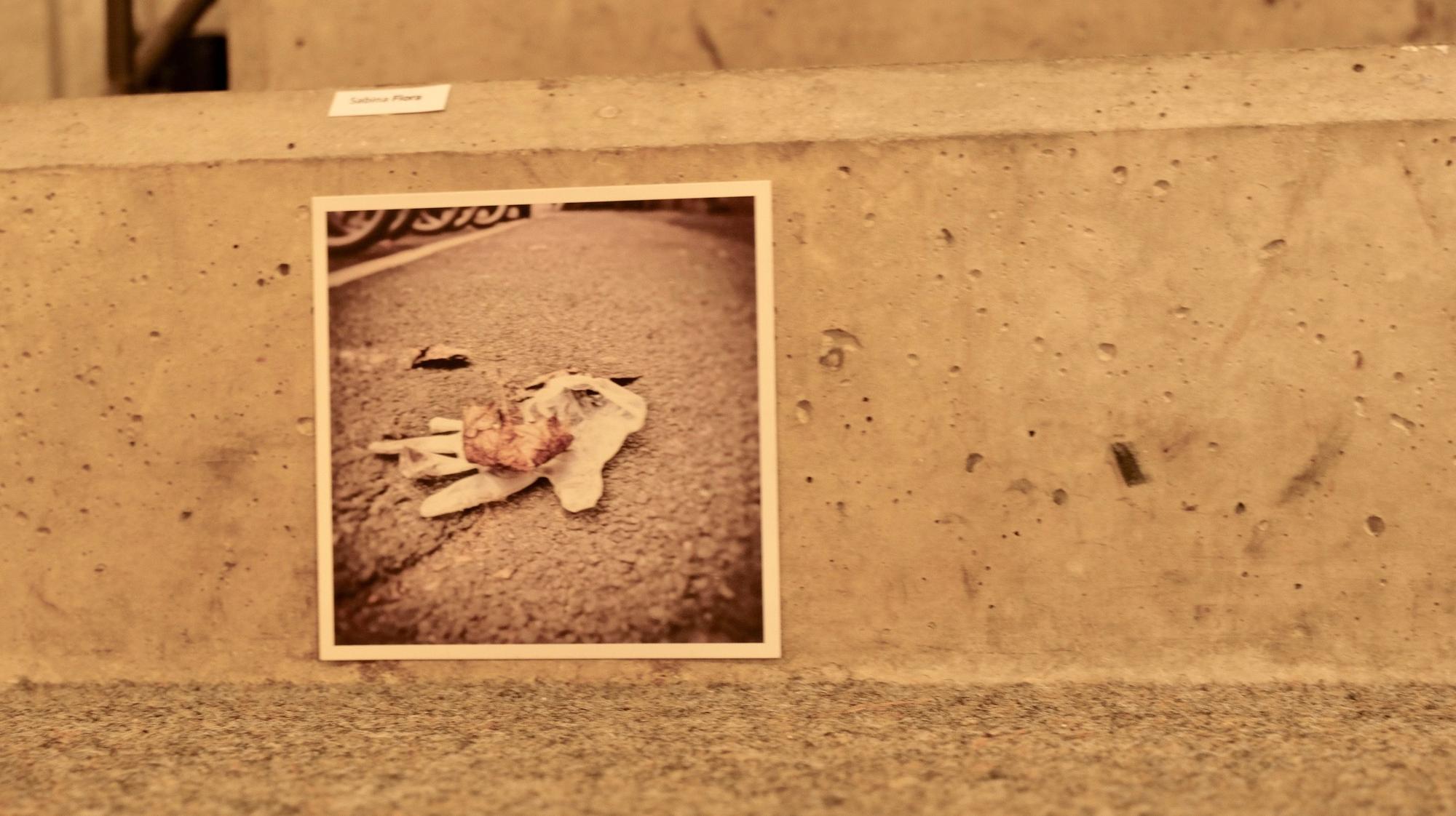 Auf einem Schwarz-Weiß-Foto ist ein einzelner Handschuh zu sehen, der verloren auf einer Straße liegt, darauf ein verwittertes Blatt.