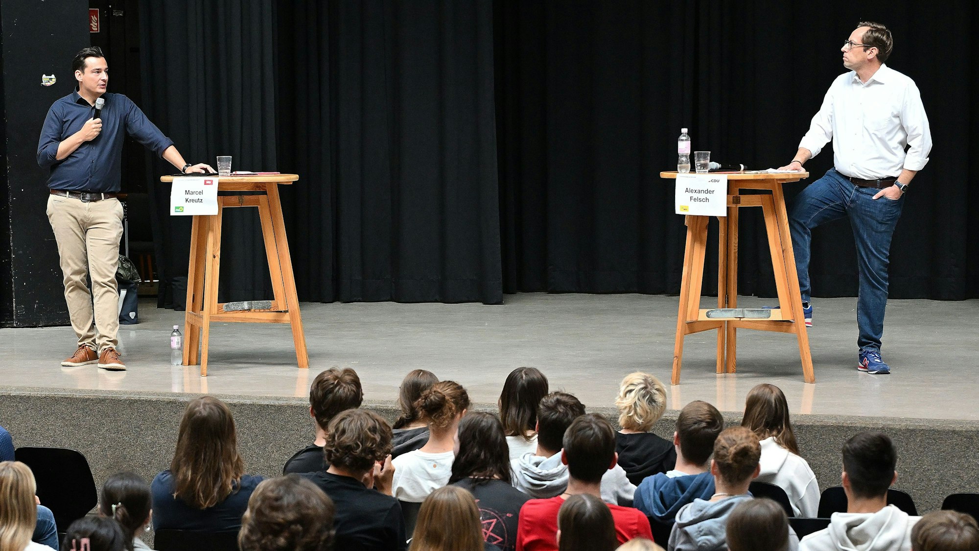 Die beiden Kandidaten stehen an Stehtischen und gucken sich an.