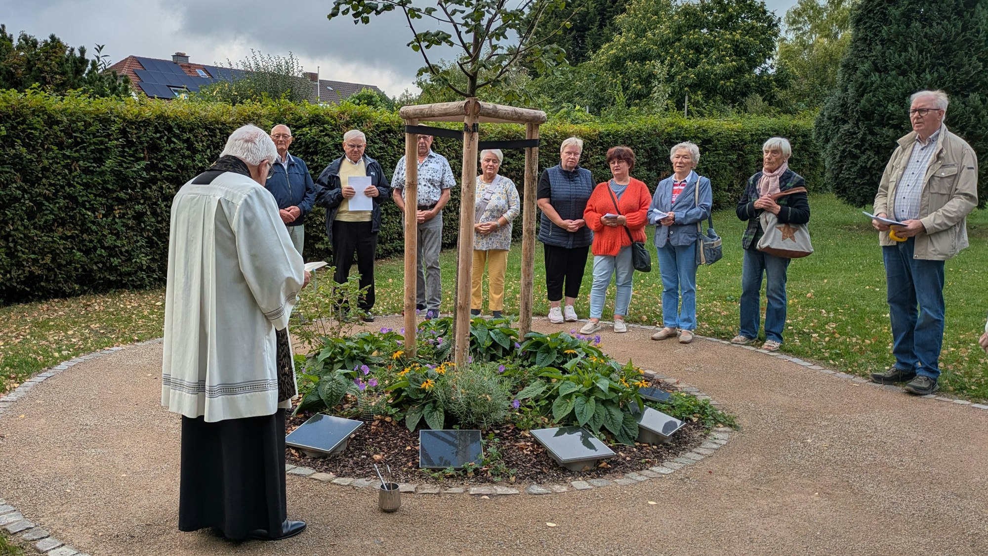 Menschen stehen um ein Urnengrabfeld an einem Baum.