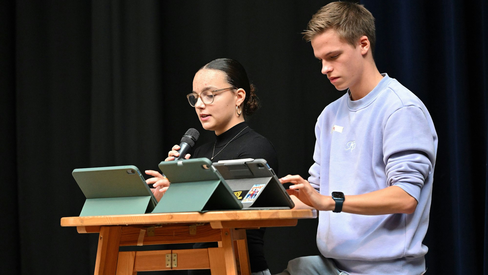 Eine Schülerin und ein Schüler stehen nebeneinander an einem Pult.